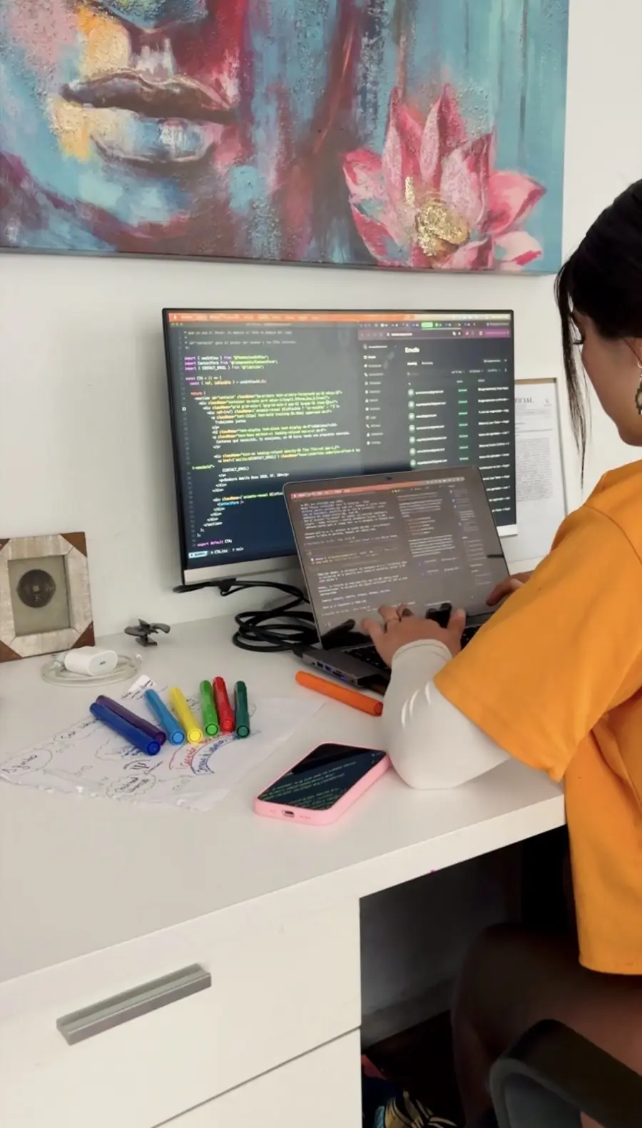 Integrante del equipo de Wisest Labs programando en su escritorio: código en el monitor y en la notebook, plumones de colores y un mapa mental a mano sobre la mesa.